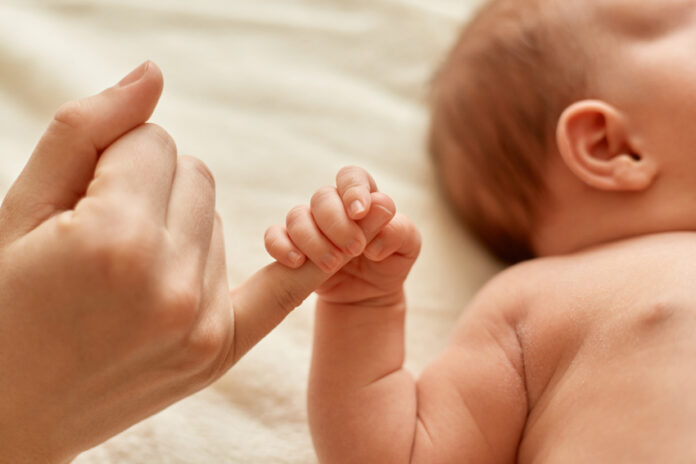 Faceless mother with naked baby, infant holding mommy's finger,
