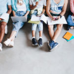 Overhead portrait of young people with laptops and smartphones, sitting together on the floor. Students writing lectures holding textbooks on their knees..