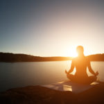 Silhouette of healthy woman is practicing yoga at mountain lake