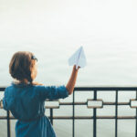 Girl launching toy paper airplane looking to lake