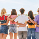 Back view group of friends, multiracial teenagers hugging on the street. Friendship concept
