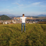 View of a male standing on a hill with his arms open while proudly looking at his hometown