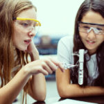 Two young girls, wearing safety goggles, in science experiment.